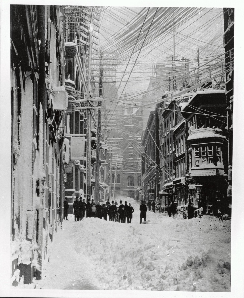 New York street in March 1888 under the Great Blizzard, with dozens of sagging telegraph and electric wires on tall poles.